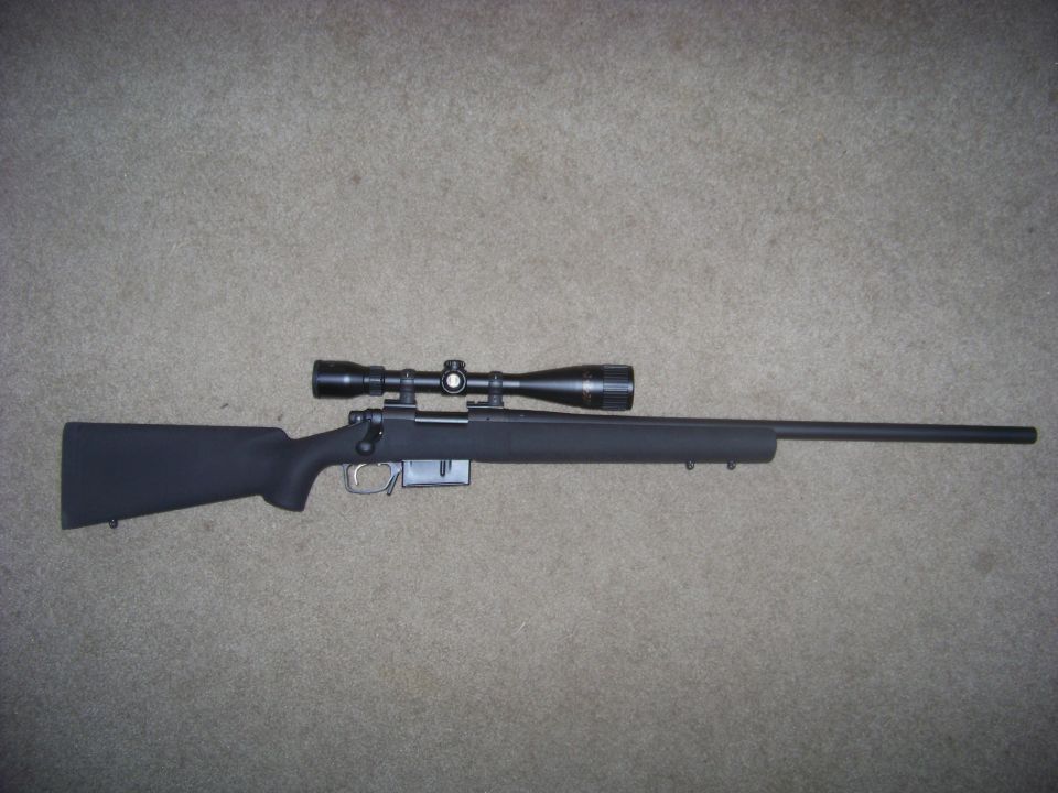 Bolt-action rifle with a scope mounted on top, resting on a carpeted surface