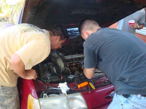 1993 Ford Taurus - Two men are working on the engine of a red 1993 Ford Taurus SHO.