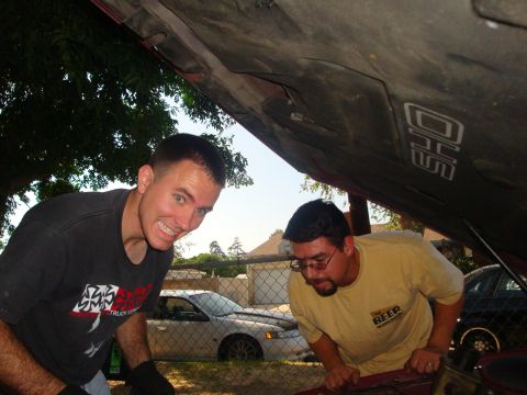 1993 Ford Taurus - Two men are working on a car's engine, with a silver sedan parked nearby.