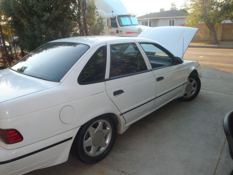 1993 Ford Taurus - A white sedan is parked outside with its hood open, a semi-truck visible in the background.