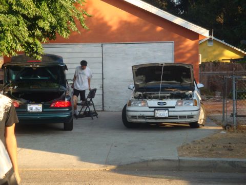 1993 Ford Taurus - Two sedans are parked in a driveway in front of a garage, one with its hood open.