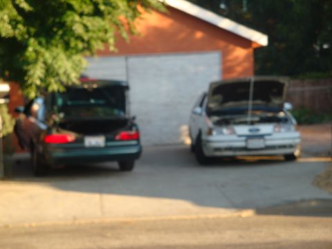 1993 Ford Taurus - Two sedans are parked in front of a garage, one with its trunk open and the other with its hood open.