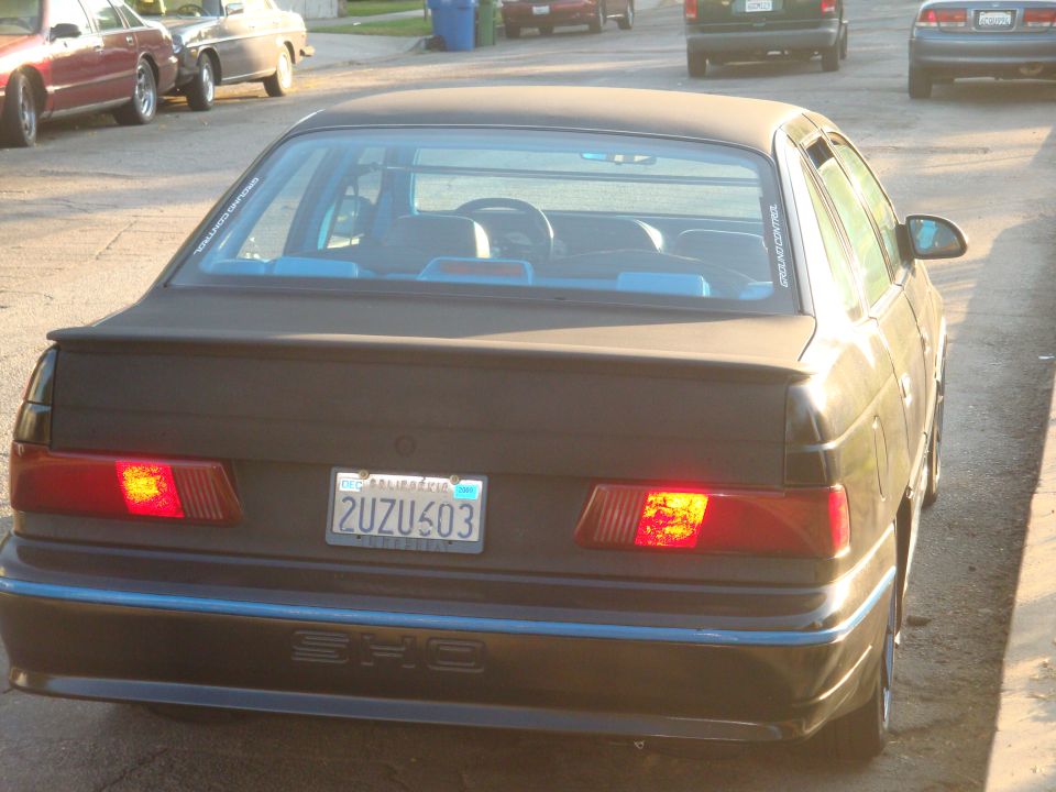 1993 Ford Taurus SHO rear view with California license plate 2UZU603. Other cars and a trash bin are visible in the background