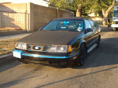 1993 Ford Taurus - A black sedan with blue accents is parked on a residential street.