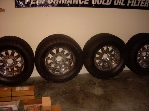 1993 Ford Bronco - Four chrome wheels with aggressive off-road tires are displayed against a wall.