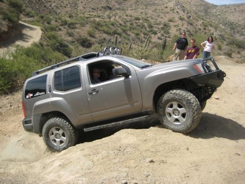 1996 Ford Bronco - Nissan Xterra navigates a steep dirt incline on an off-road trail with spectators present spectators.