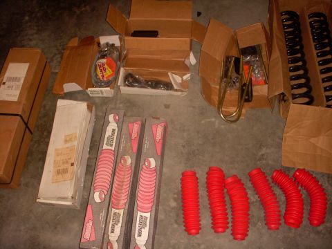 1993 Ford Bronco - Various vehicle parts, including shocks, springs, and red protective boots, are laid out on a concrete floor.