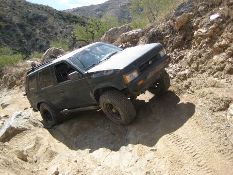 1996 Ford Bronco - Nissan Pathfinder tackling a challenging off-road course with steep inclines and rocky terrain.