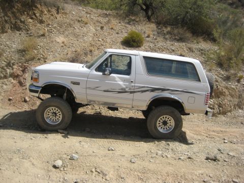 1996 Ford Bronco - A white Ford Bronco navigates a dusty, rocky trail in a dry, arid environment.
