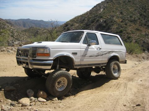 1996 Ford Bronco - This lifted 1996 Ford Bronco navigates a rocky, off-road trail under a clear sky.