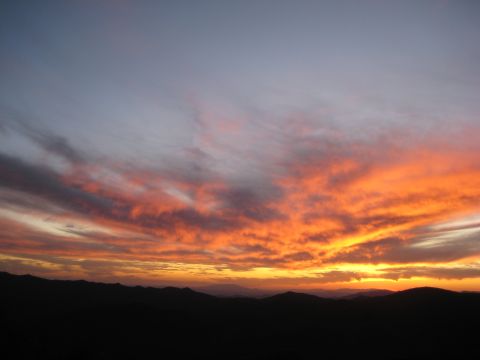 1996 Ford Bronco - A vibrant sunset paints the sky with fiery colors above a silhouetted mountain range, with website text visible.