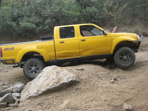 1996 Ford Bronco - A yellow Nissan pickup truck is shown off-roading on a dirt path with large rocks.