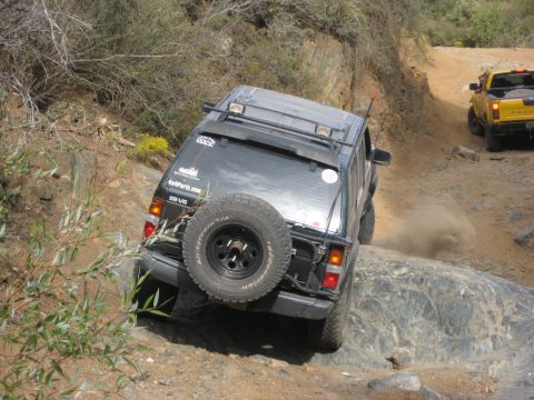 1996 Ford Bronco - A dark SUV navigates a rocky off-road trail, with a yellow truck following behind.