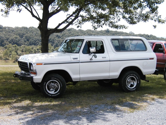 White full-size Ford Bronco with hardtop parked in profile on grass under a tree