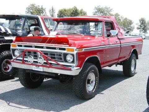 1994 Ford Bronco - A red Ford pickup truck from the 1970s is parked next to another vehicle, a prominent front brush guard.