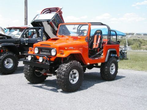 1994 Ford Bronco - An orange Toyota Land Cruiser FJ40 is parked next to a black truck with its bed raised.