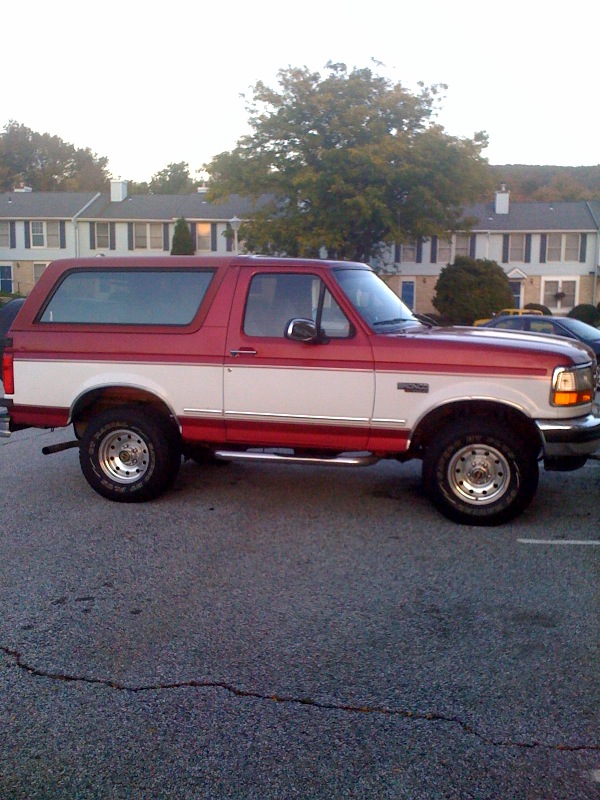 Side view of red and white Ford Bronco SUV parked in lot in front of townhouses