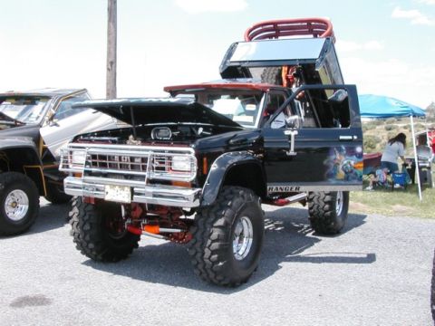 1994 Ford Bronco - This heavily modified truck features custom artwork on the door and a raised bed rack, parked next to another off-road vehicle.