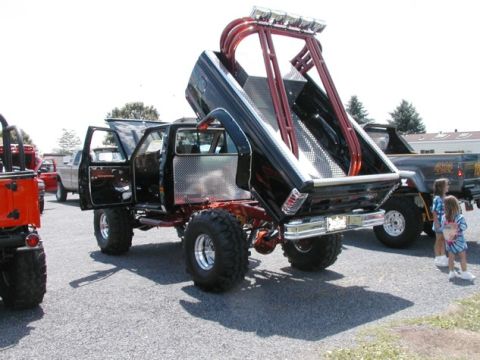 1994 Ford Bronco - Custom pickup truck with dump bed and roll cage, parked outdoors with other vehicles and people.