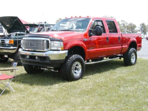 1994 Ford Bronco - A red Ford F-250 Super Duty pickup truck is parked on a grassy field, with another vehicle visible to its left.