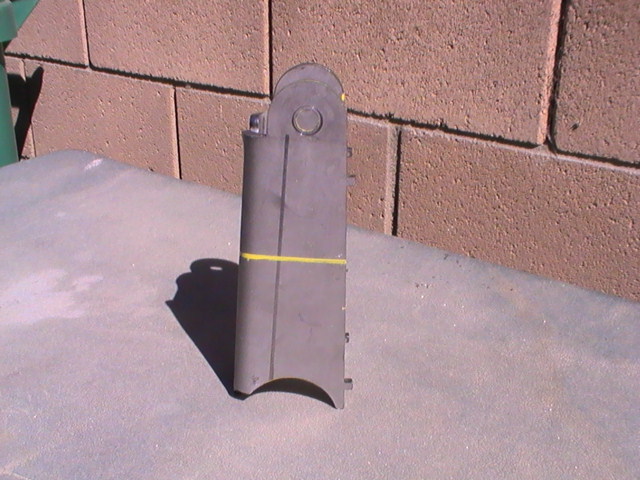 Metal bracket with a yellow line drawn around it, resting on a textured surface