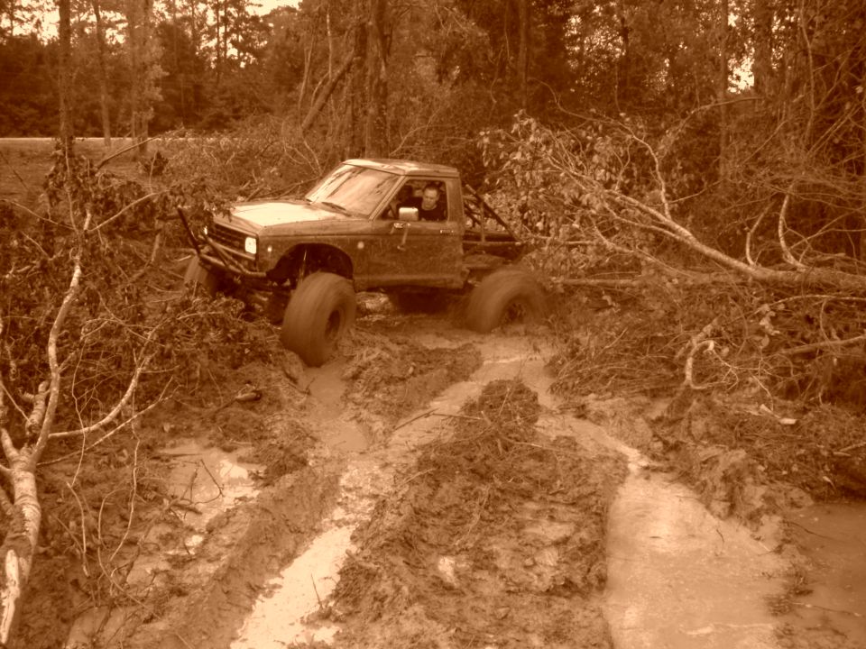 Mud-covered off-road truck with large tires stuck in mud and branches