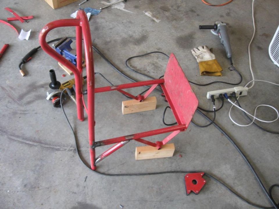 Red welding cart frame on wooden blocks with grinder and gloves