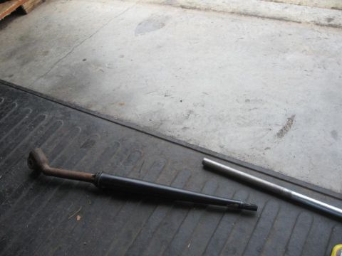 1995 Ford F-150 - A drive shaft and a metal tube lie on a ribbed surface next to a concrete floor.