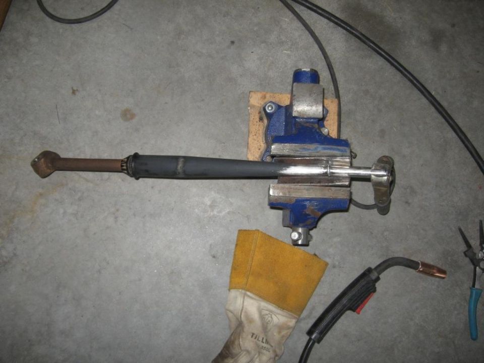 Drive shaft clamped in a blue vise with welding equipment nearby
