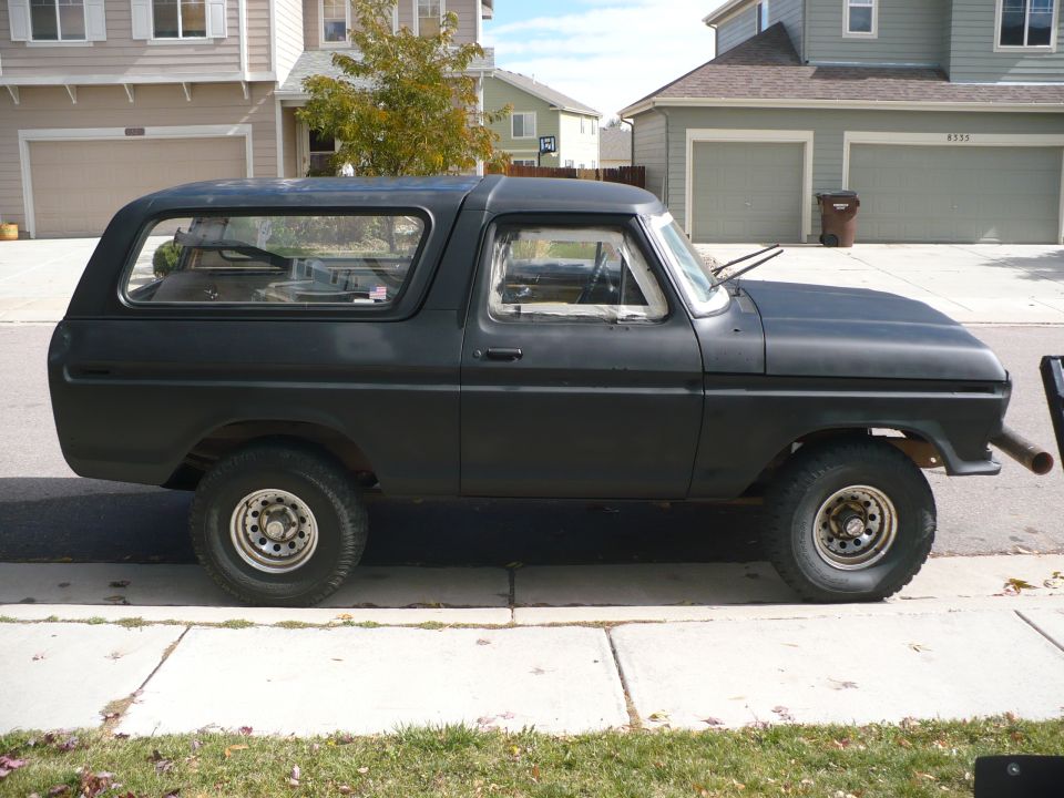 Black 1978 Ford Bronco parked on a sidewalk, side view, matte paint, some rust visible