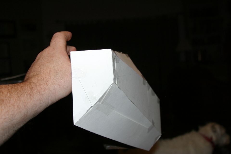 Hand holding a white cardboard model of a car bumper, taped together