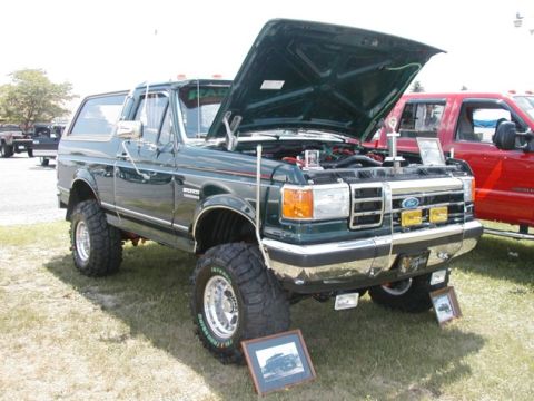 1994 Ford Bronco - This lifted green Ford Bronco displays its engine with the hood open, parked next to a red truck.