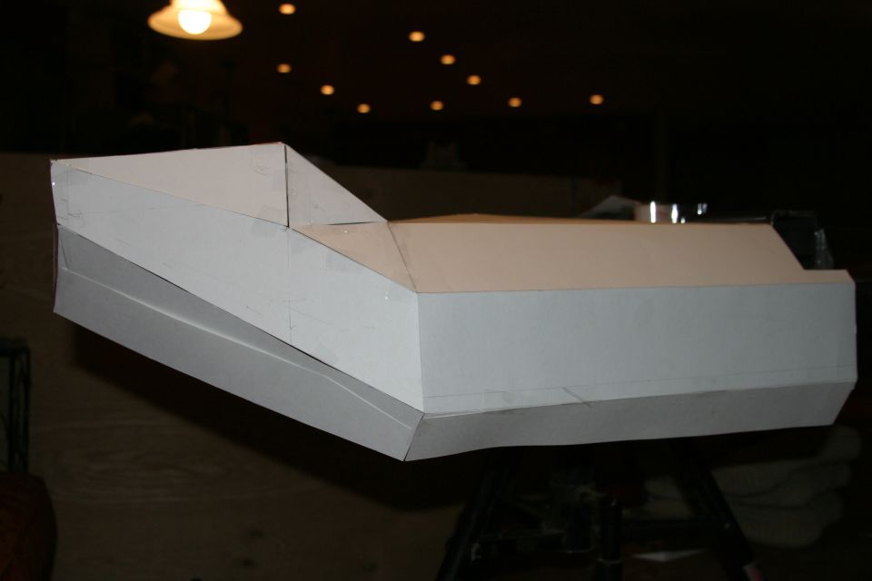 White cardboard mockup of an angular vehicle bumper on a stand in a dark shop