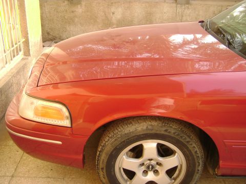 1998 Ford Crown Victoria - Front view of a red 1998 Ford Crown Victoria, showing the fender and headlight assembly.