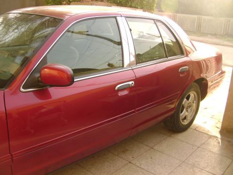 1998 Ford Crown Victoria - Side profile of a red 1998 Ford Crown Victoria sedan parked on a tiled surface.