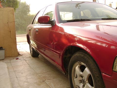 1998 Ford Crown Victoria - A red 1998 Ford Crown Victoria is parked on a tiled surface, viewed from the front quarter angle.