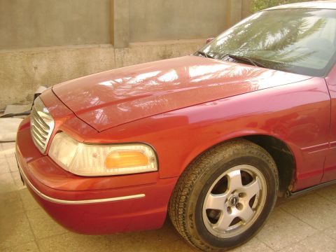 1998 Ford Crown Victoria - The front passenger side of a red sedan is shown, its headlight, grille, and wheel.