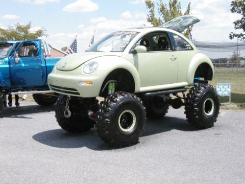 1994 Ford Bronco - A heavily modified Volkswagen Beetle sits on oversized tires next to a blue pickup truck.