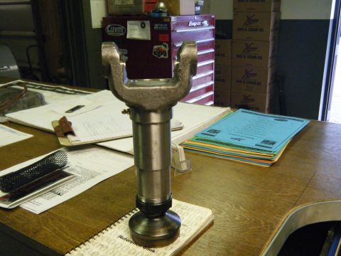 1978 Ford Bronco - A metal driveshaft U-joint sits on a desk, surrounded by documents and workshop equipment.