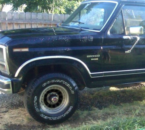 1986 Ford Bronco - A black 1986 Ford Bronco is shown from the front quarter panel to the door, with chrome accents and Goodyear Wrangler tires.