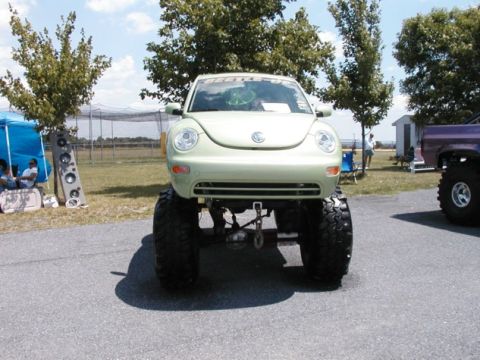 1994 Ford Bronco - A heavily modified Volkswagen New Beetle with oversized tires is displayed outdoors, with other vehicles and tents in the background.
