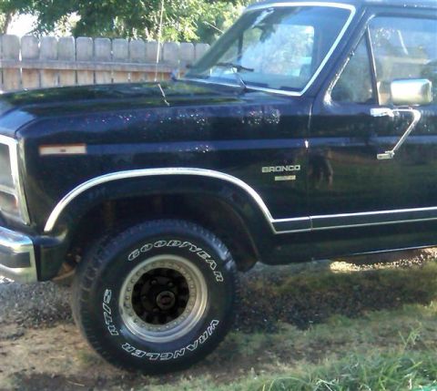 1986 Ford Bronco - This black Ford Bronco shows its front fender and door, with chrome trim and fender flares visible.