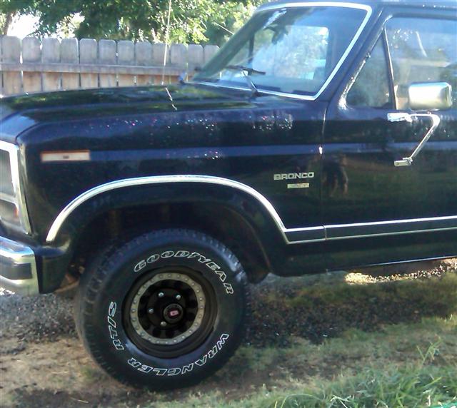 Black 1986 Ford Bronco, front fender and door visible. Goodyear Wrangler tires on aftermarket wheels