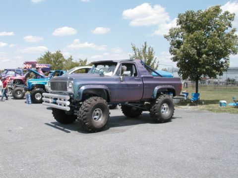 1994 Ford Bronco - Several modified trucks are lined up at an outdoor event under a partly cloudy sky.