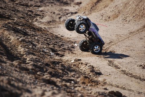 1990 Ford Bronco - RC monster truck flips over on a sandy terrain.