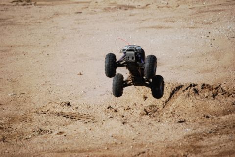 1990 Ford Bronco - RC rock crawler jumps over a dirt mound, kicking up dust.