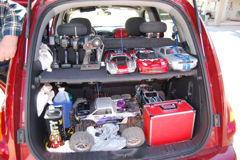 1990 Ford Bronco - The trunk of a red car is packed with multiple remote control cars, controllers, and various supplies for them.
