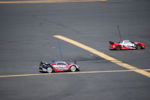 1990 Ford Bronco - Two remote control cars race on a track, one in the foreground and another in the background.