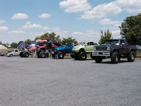 1994 Ford Bronco - Several custom-built, lifted vehicles are parked in a lot under a partly cloudy sky.