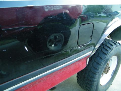 1990 Ford F-350 - The side of a 1990 Ford F-350 pickup truck, a fuel door and visible damage to the lower body trim.